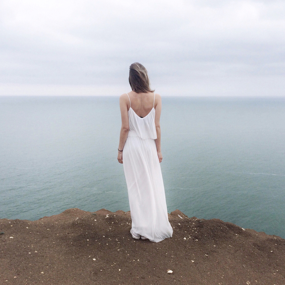 Woman in White Spaghetti Strap Dress Standing on Cliff